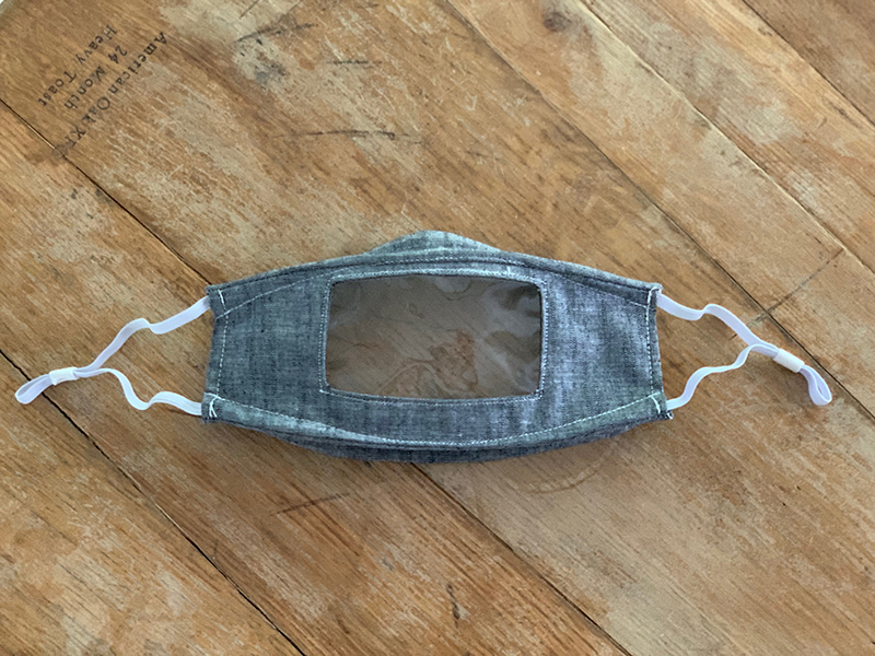 A handmade Read My Lips mask with a transparent window, laid on a wooden table
